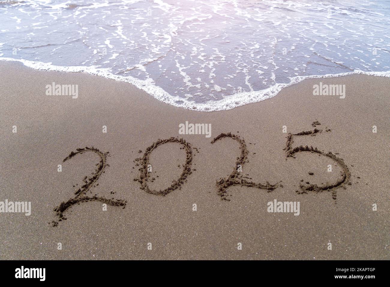 Text Happy New Year 2025 on a sandy sea beach with a small wave. Abstract background photo of the upcoming New Year 2023 Stock Photo