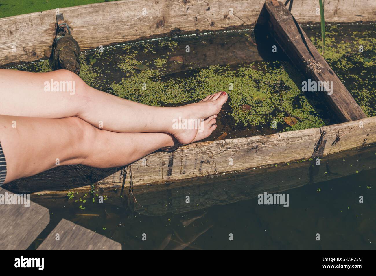 Elongated female legs lean on old submerged boat Stock Photo