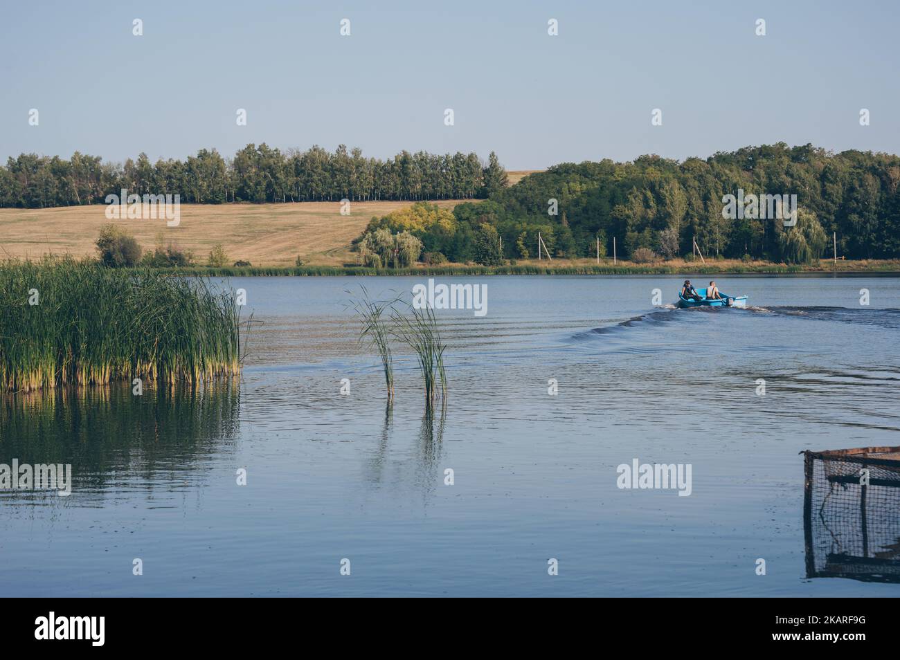 Two fyshemen in motor boat sails dissecting waves on river again Stock Photo