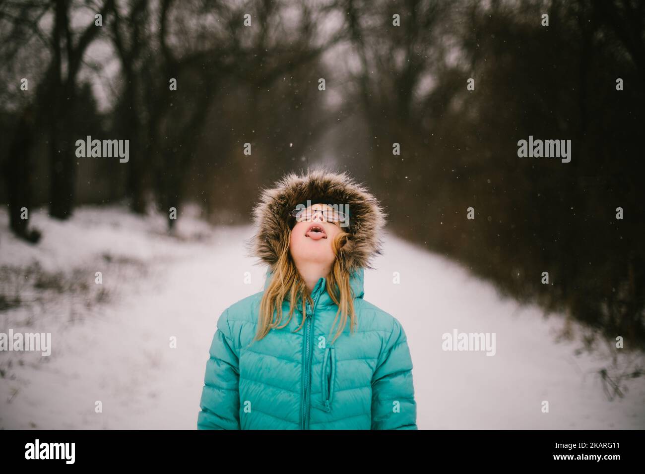 Blond girl catches snowflakes on tongue in forest snow fall Stock Photo