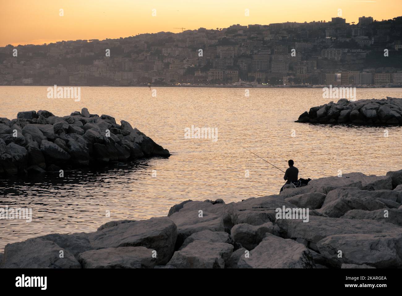 Silhouette of a man fishing on rocks at seafront of Naples Stock Photo ...