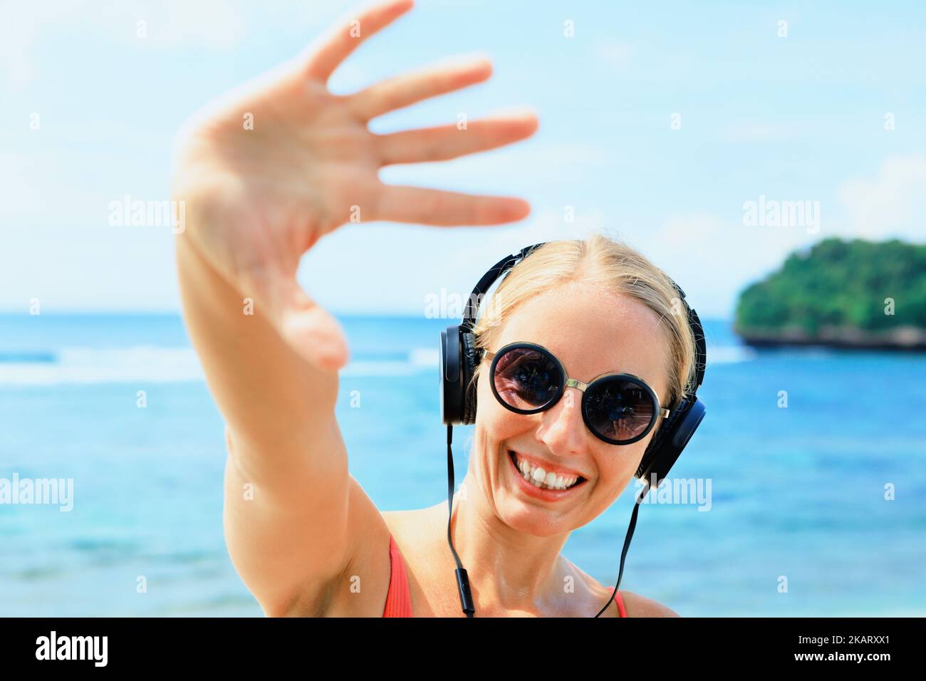 Young positive girl in headphones and sunglasses listening music and dancing with fun at tropical beach party. Travel family lifestyle, recreational a Stock Photo