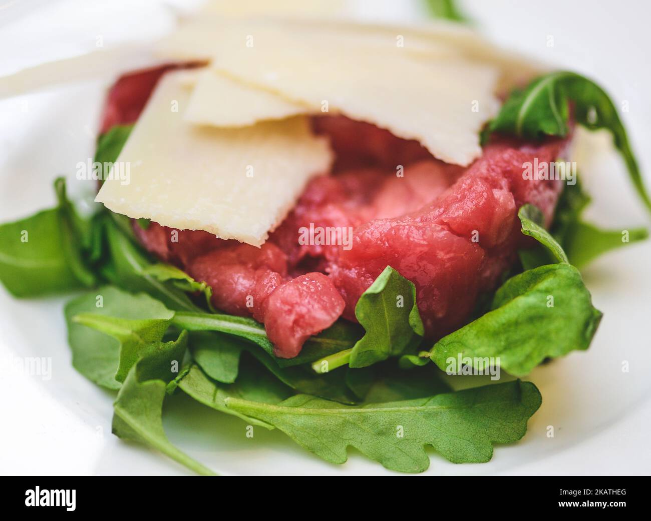 Beef  tartare or tartar steak, dish of raw ground minced beef with parmesan cheese flakes and rocket leaves just served in a white plate, close up Stock Photo