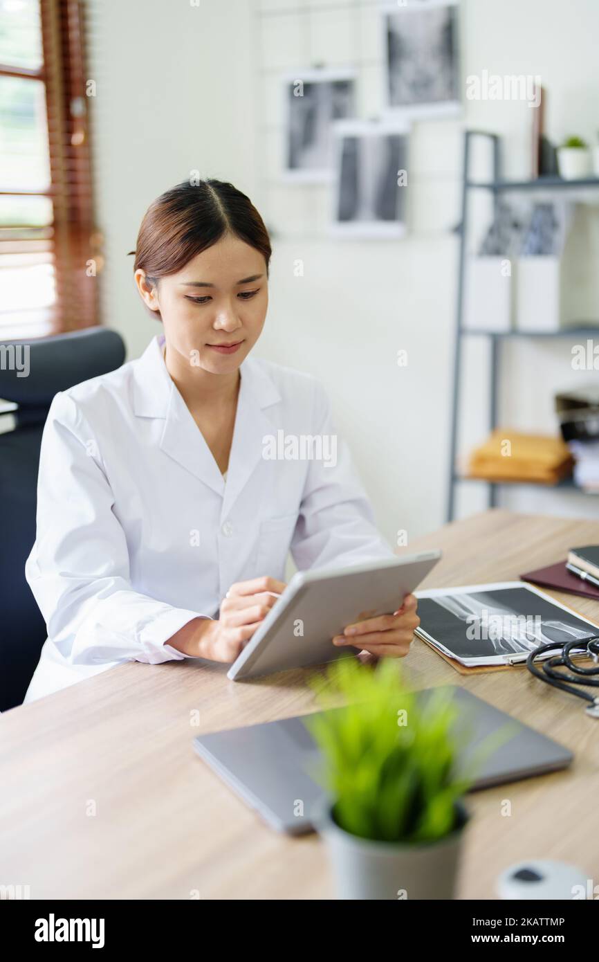 An Asian female doctor is using a tablet computer to analyze patient symptoms before treatment Stock Photo
