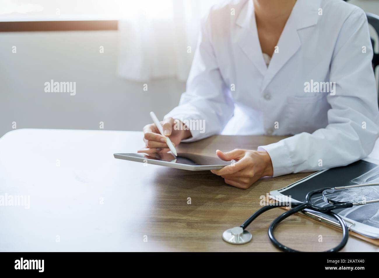 An Asian female doctor is using a tablet computer to analyze patient symptoms before treatment Stock Photo