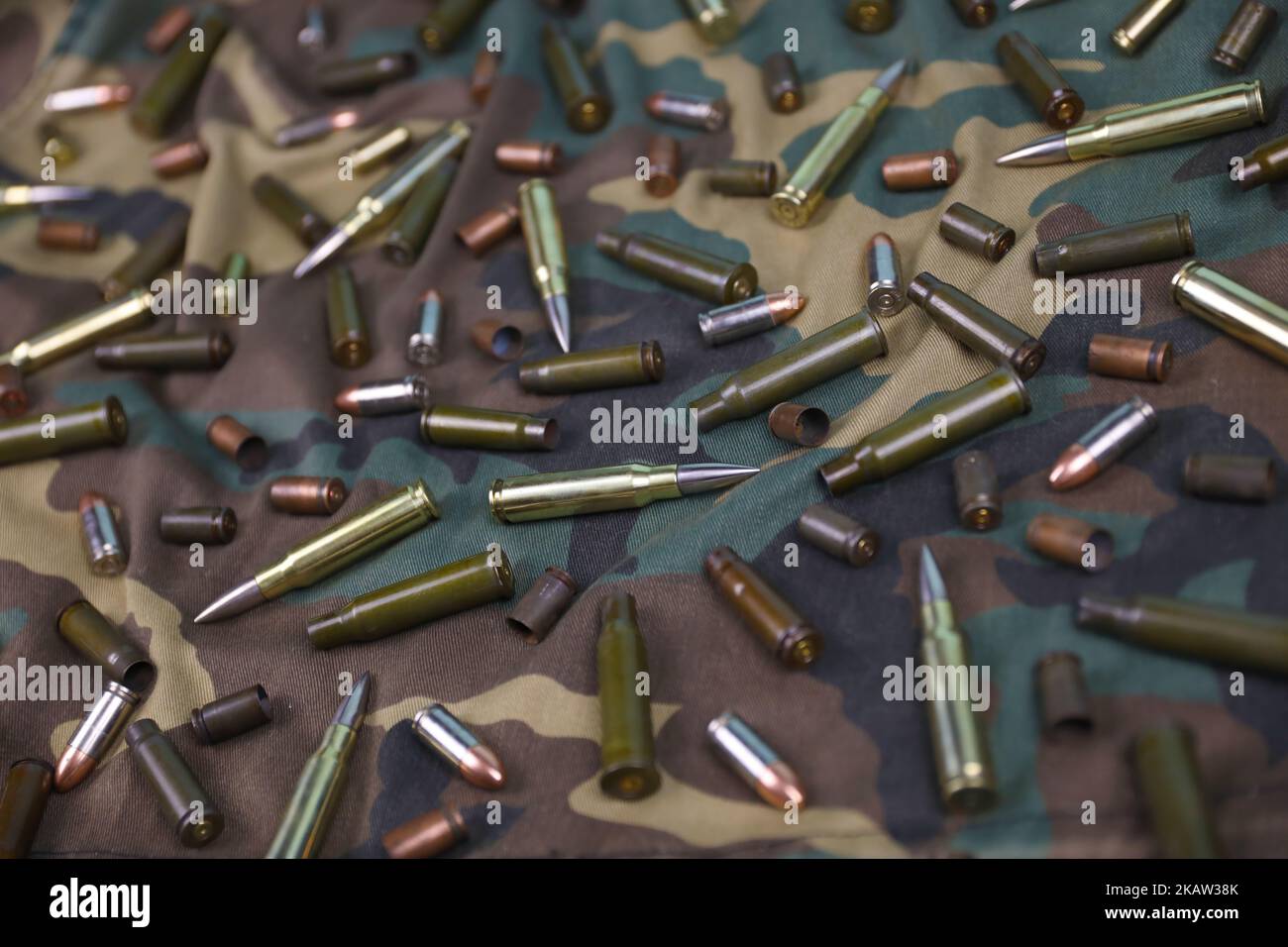 Many rifle bullets and cartridges on dark camouflage background. Concept of war action or hunting Stock Photo