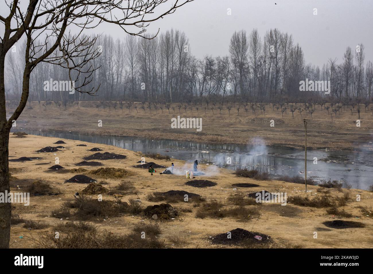 A Kashmiri woman burn the water chestnut shells to obtain charcoal which will be later used as fuel in kangris, an earthenware container with an outer encasement of wickerwork, filled with burning coal and normally carried under the clothing for heat in winter months, on January 05, 2018 in Narbal, north of Srinagar, the summer capital of Indian Administered Kashmir, India. Water chestnuts are a major crop for people living near Wular lake , Asia's second largest freshwater lake. Wular, looks more like a flat marshy plain than a large lake in winters, as the water level recedes entire families Stock Photo