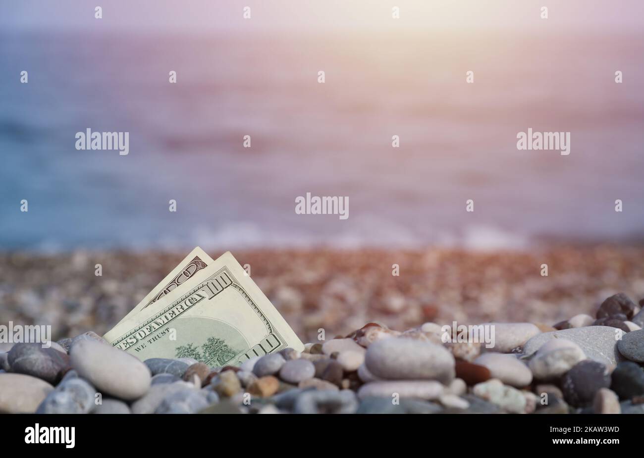 Hundred dollars half covered with round rocks lie on beach close up. Dollar bills partially buried in sea shore stones. Concept finance money holiday Stock Photo