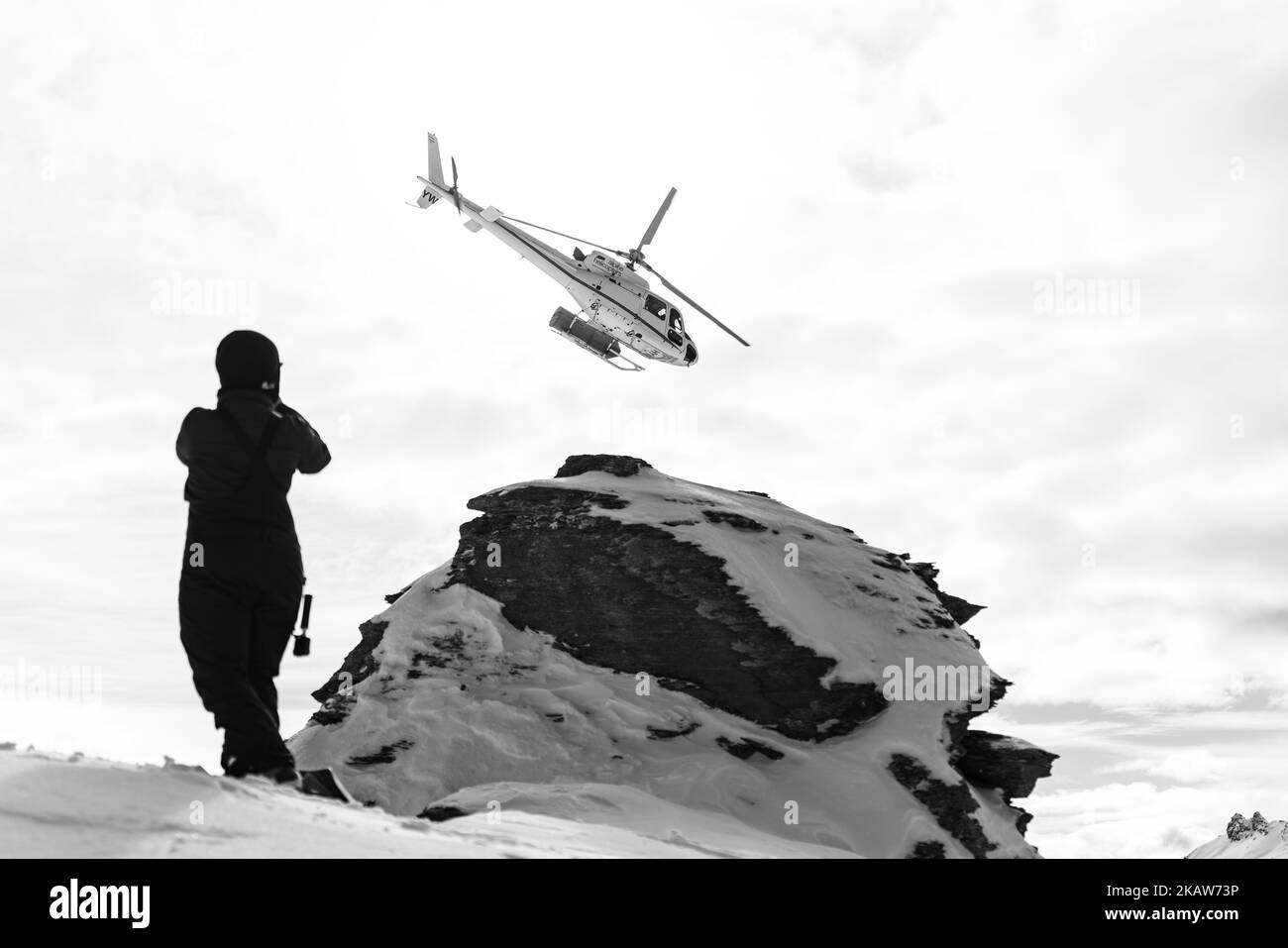 A silhouette grayscale shot of a person watching Heliskiing drop off on ...
