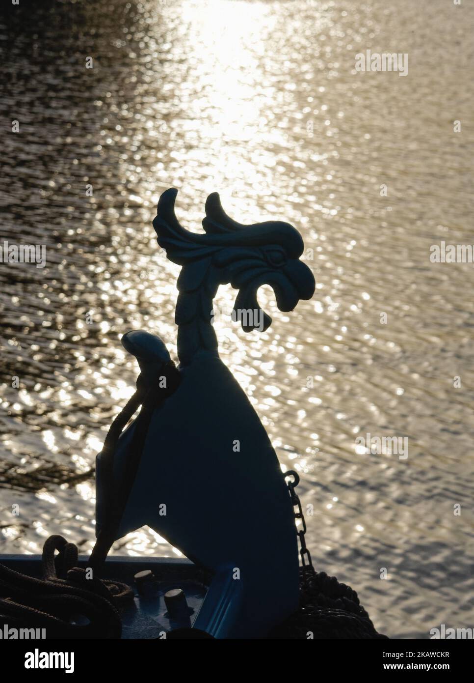 Silhouette of a dragon figurehead on a boat against a background of strong sunlight reflecting on a river surface, Shepperton UK Stock Photo