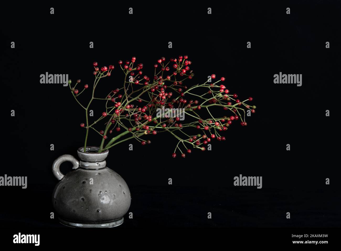 Bunch of red berries on the table in a grey vase.  Stock Photo