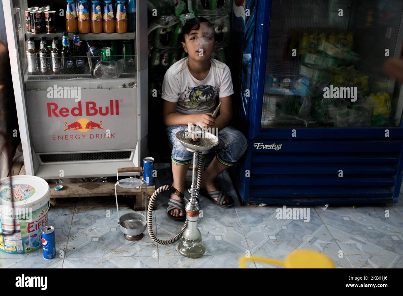 A boy working in a supermarket in Qamishli, Syria smokes a hookah in the shop during a break (Photo by Sebastian Backhaus/NurPhoto) Stock Photo