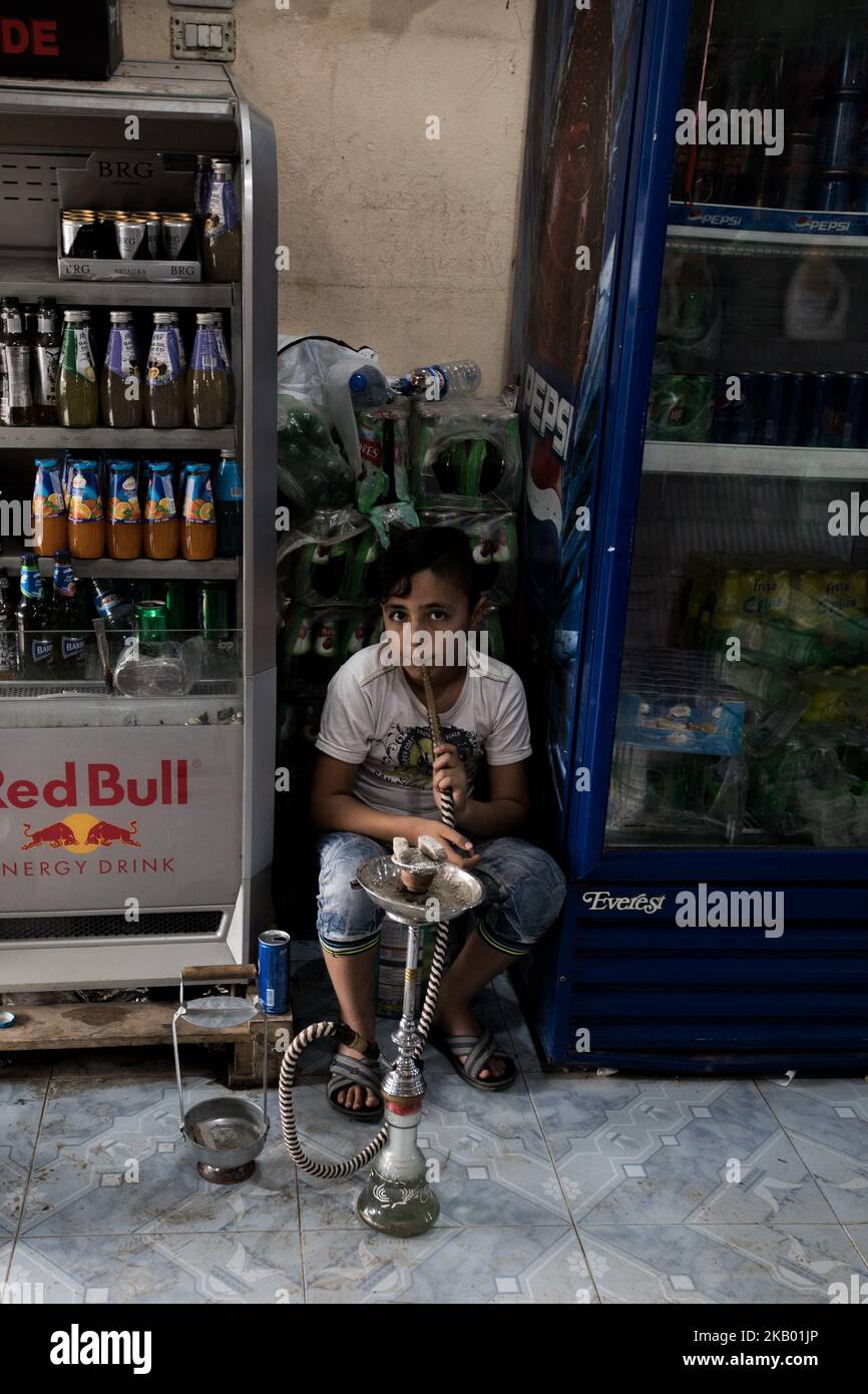 A boy working in a supermarket in Qamishli, Syria smokes a hookah in the shop during a break (Photo by Sebastian Backhaus/NurPhoto) Stock Photo