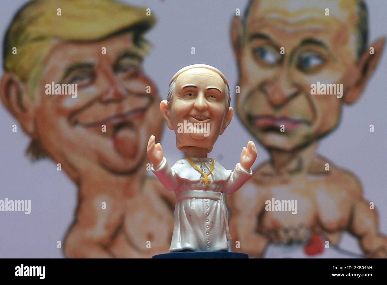 A mini size Pope Francis Bobble head in front of a watercolor caricature which features President Donald Trump and President Vladimir Putin, made by an Irish Artist Ray Sherlock, on display at Dublin's Balla Ban Art Gallery. The gallery owner Frank O'Dea will be giving them out for free with every purchase made during the Pope's visit to Ireland. Pope Francis is due to visit Ireland from August 21 to 26 in what will be the first papal visit since Pope John Paul II came in 1979. On Wednesday, July 18 2018, in Dublin, Ireland. (Photo by Artur Widak/NurPhoto)  Stock Photo