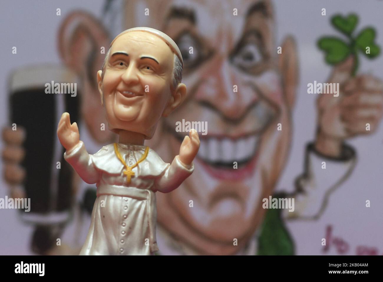 A mini size Pope Francis Bobble head in front of a watercolor caricature which features Pope Francis hoding a pint of Guinness and shamrock, made by an Irish Artist Ray Sherlock, on display at Dublin's Balla Ban Art Gallery. The gallery owner Frank O'Dea will be giving them out for free with every purchase made during the Pope's visit to Ireland. Pope Francis is due to visit Ireland from August 21 to 26 in what will be the first papal visit since Pope John Paul II came in 1979. On Wednesday, July 18 2018, in Dublin, Ireland. (Photo by Artur Widak/NurPhoto)  Stock Photo