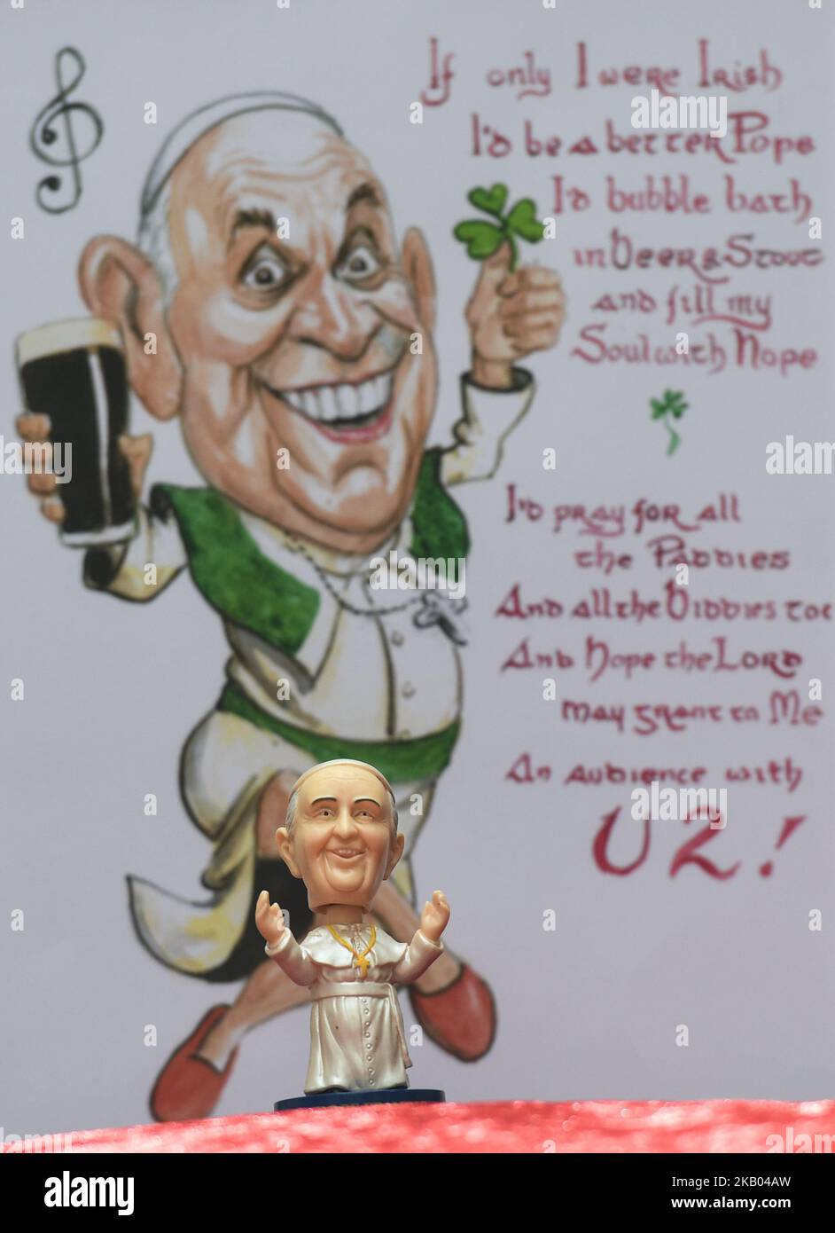 A mini size Pope Francis Bobble head in front of a watercolor caricature which features Pope Francis hoding a pint of Guinness and shamrock, made by an Irish Artist Ray Sherlock, on display at Dublin's Balla Ban Art Gallery. The gallery owner Frank O'Dea will be giving them out for free with every purchase made during the Pope's visit to Ireland. Pope Francis is due to visit Ireland from August 21 to 26 in what will be the first papal visit since Pope John Paul II came in 1979. On Wednesday, July 18 2018, in Dublin, Ireland. (Photo by Artur Widak/NurPhoto)  Stock Photo