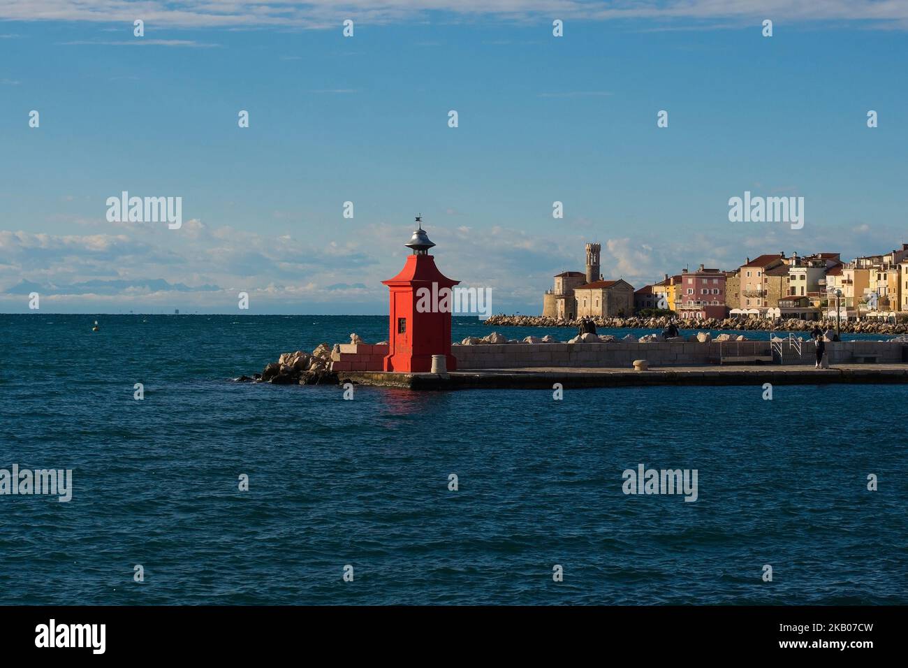 A red lighthouse on the waterfront of the historic medieval town of Piran on the coast of Slovenia. Background right is the Our Lady of Health Church Stock Photo