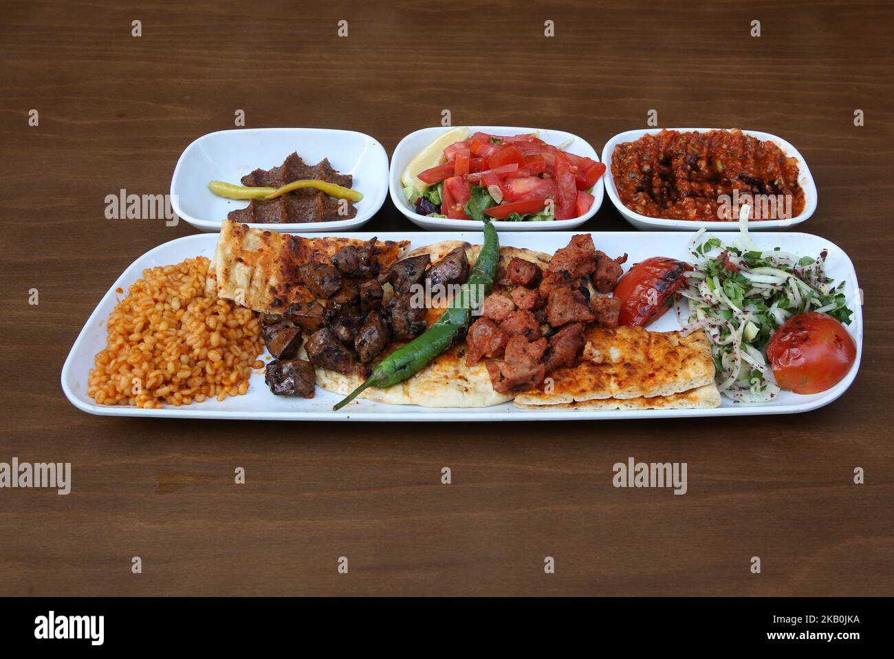Liver kebab and lamb shish kebab are on the plate, accompanied by salad, spicy paste and raw meatballs Stock Photo