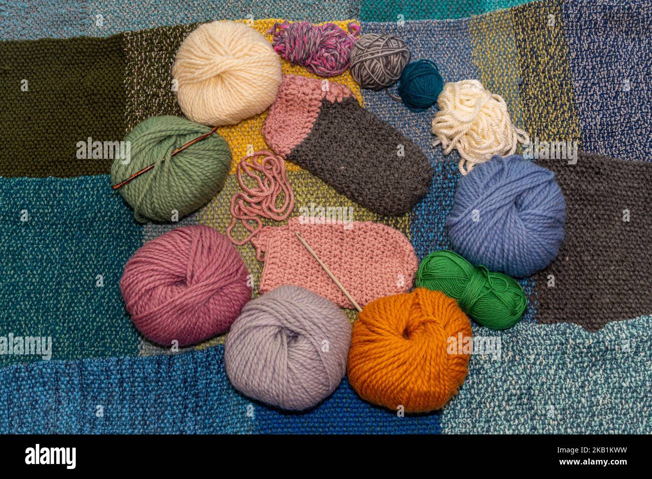 Variety of balls of wool for crochet and knitting on a warm, knitted background with woolen slippers in the making in the middle Stock Photo