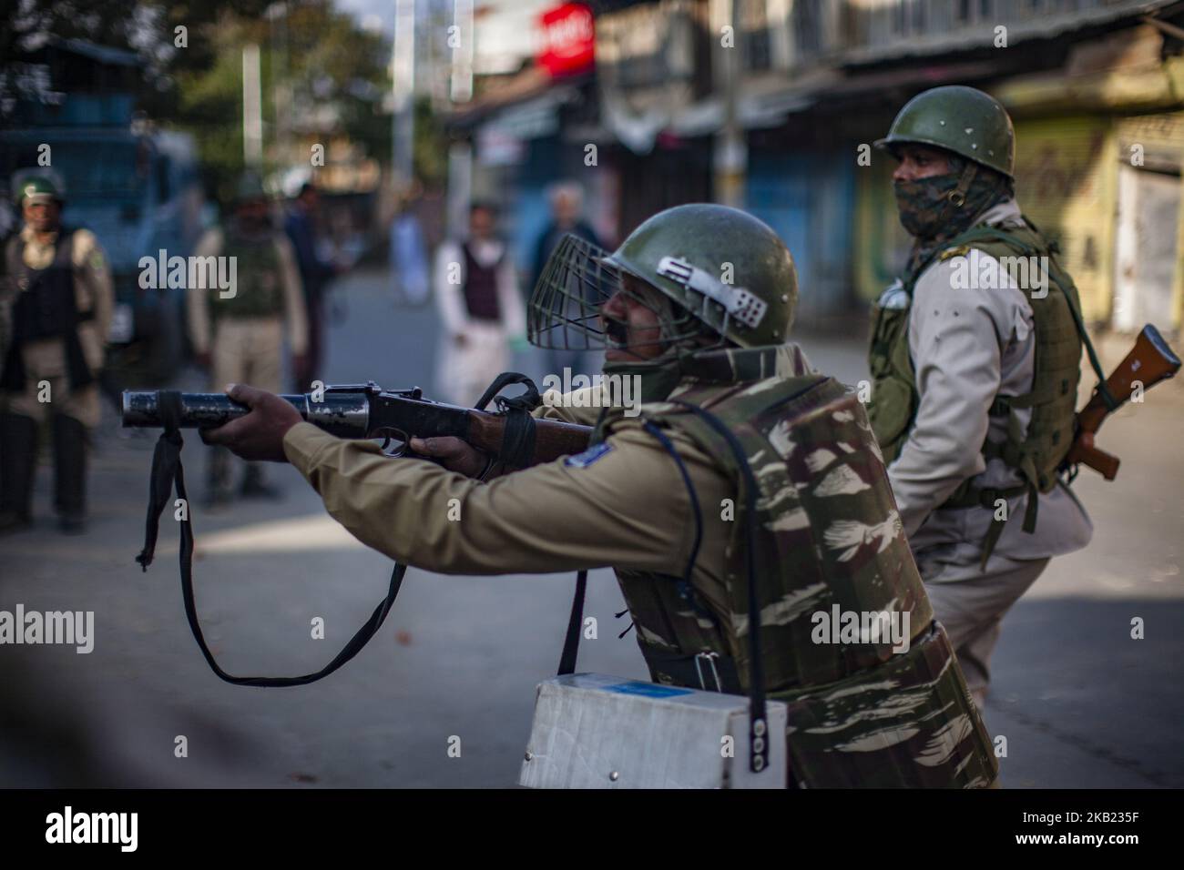 An Indian paramilitary trooper aims his gun towards Kashmiri protesters during a protest against the killing of a Kashmiri rebel commander on October 12, 2018 in Srinagar, the summer capital of Indian administered Kashmir, India.Kashmiri youth clashed with Indian government forces who were deployed in strength in different parts of Srinagar on Friday to prevent protests against the killing of a Kashmiri rebel commander in Kupwara district of Indian-administered Kashmir the previous day. Manan Wani, who had quit his doctorate in Geology at an Indian university to join the Hizb-ul-Mujahideen mil Stock Photo