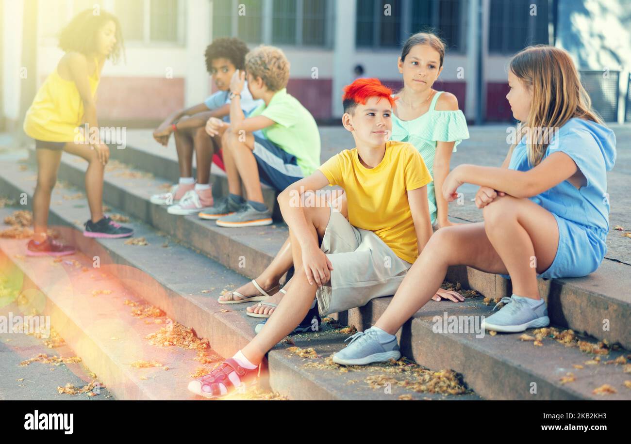Positive tweenagers friendly blabbing while sitting on steps outdoors Stock Photo