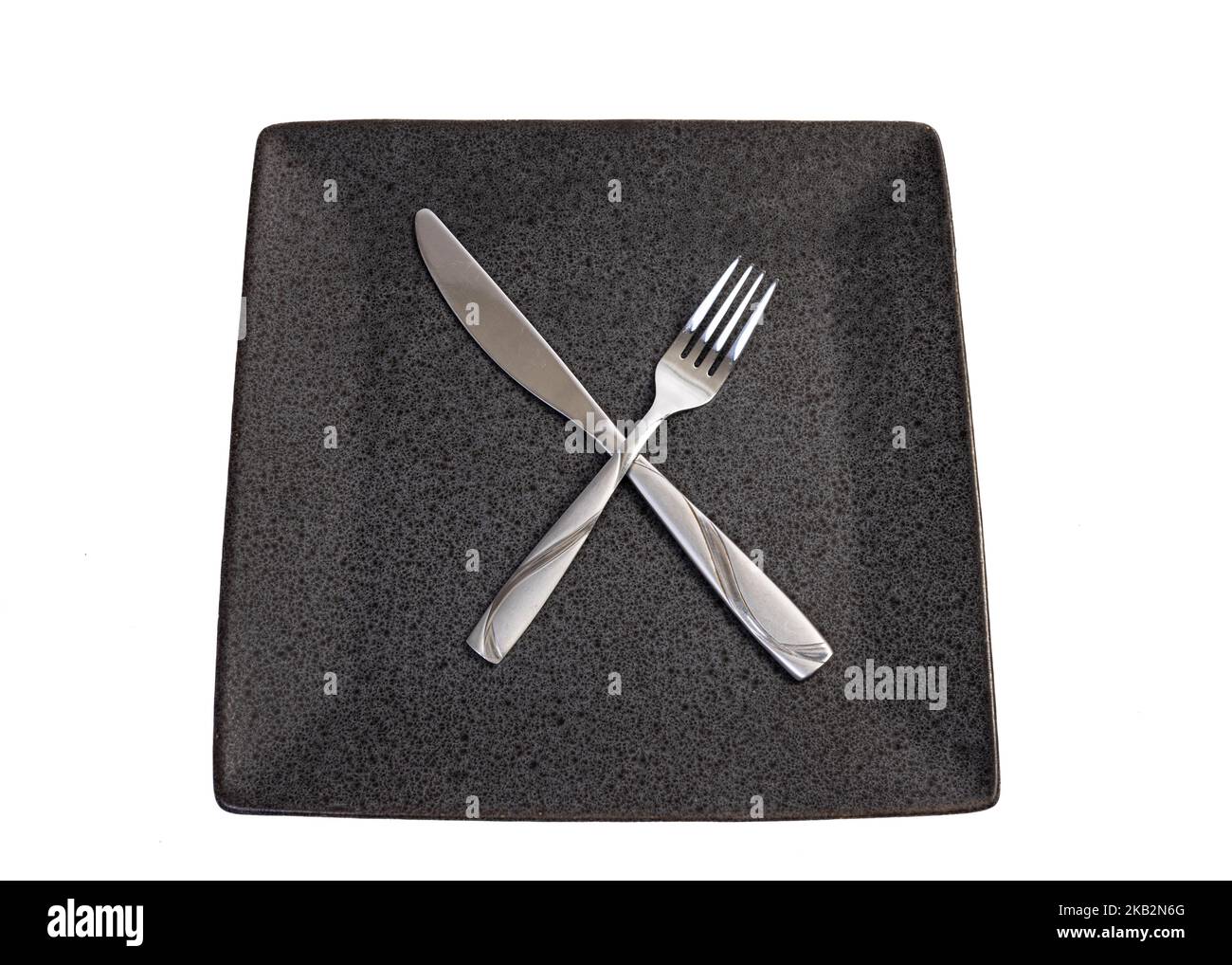 overhead shot of fork and knife crossed on square plate on a white