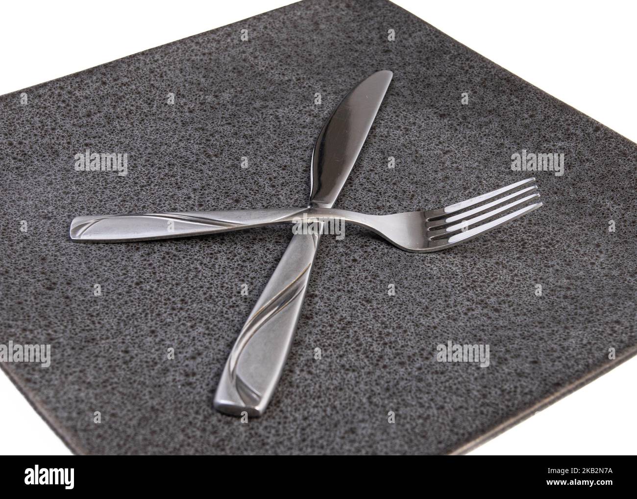 shot of fork and knife crossed on square plate on a white background