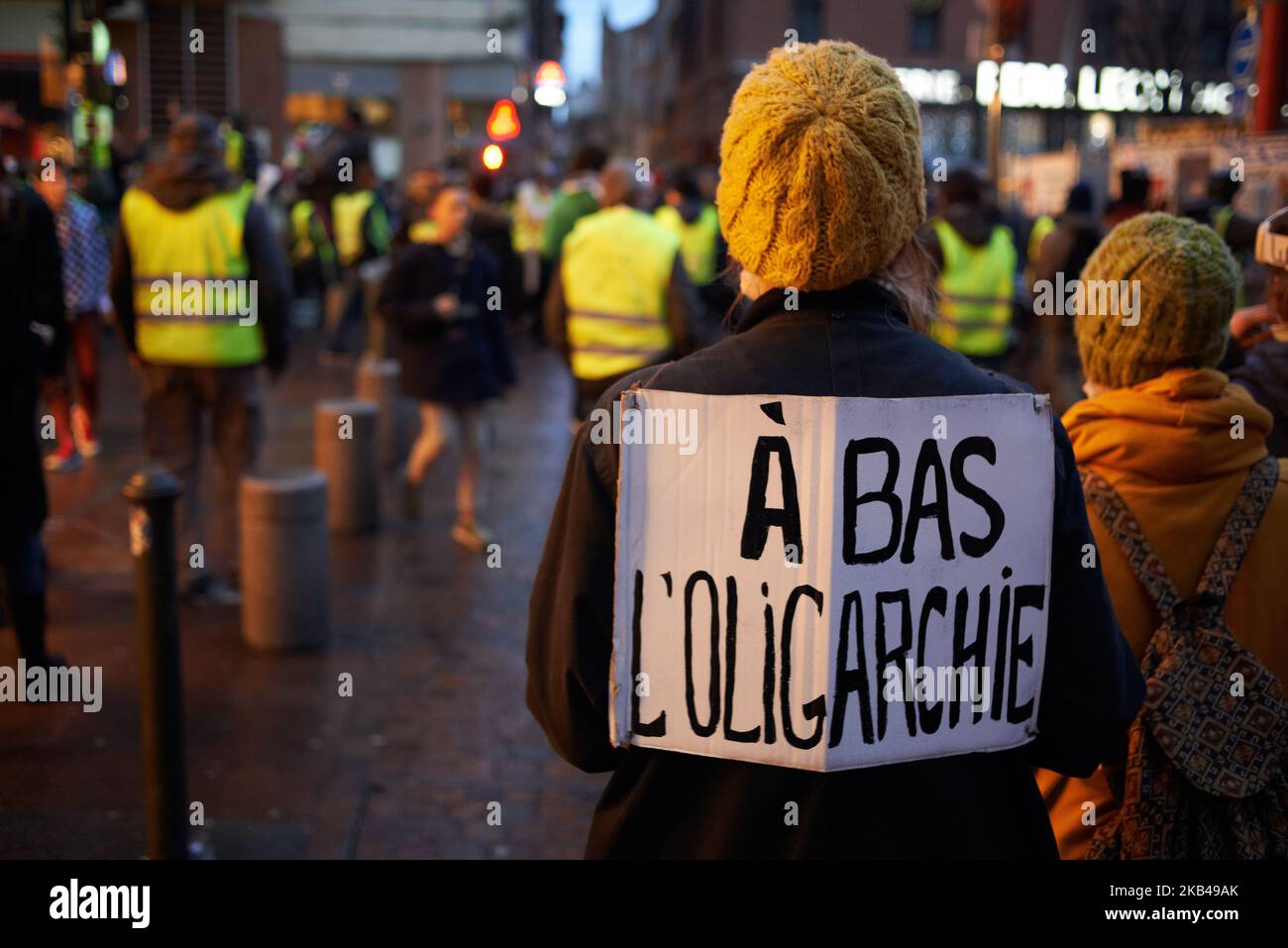 A Yellow Vest walks with a placard reading 'Down with oligarchy'. Act VI dubbed 'Revolt' of the Yellow Vest movement begun peacefully but the protest turned rapidly to riots for hours. Gendarmerie Mobile and riot police launched volleys of tear gas canisters, fired dozens rounds of flashballs and used two police water cannons. The Yellow Jackets movement begun on November 17th by a protest against the rise of taxes on oil products. The rise of taxes was the detonator of their wrath against French President Macron and his governement and their demand of his resignation.Toulouse. France. Decembe Stock Photo