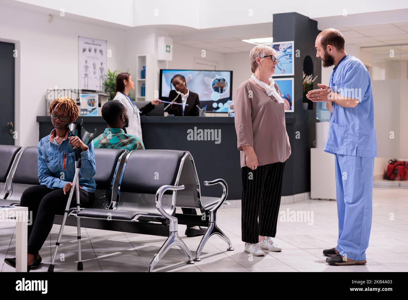 Elderly woman receiving instructions from general practitioner in hospital waiting room. African american receptionist multitasking at clinic lobby. Consistent hospital emergency room. Stock Photo
