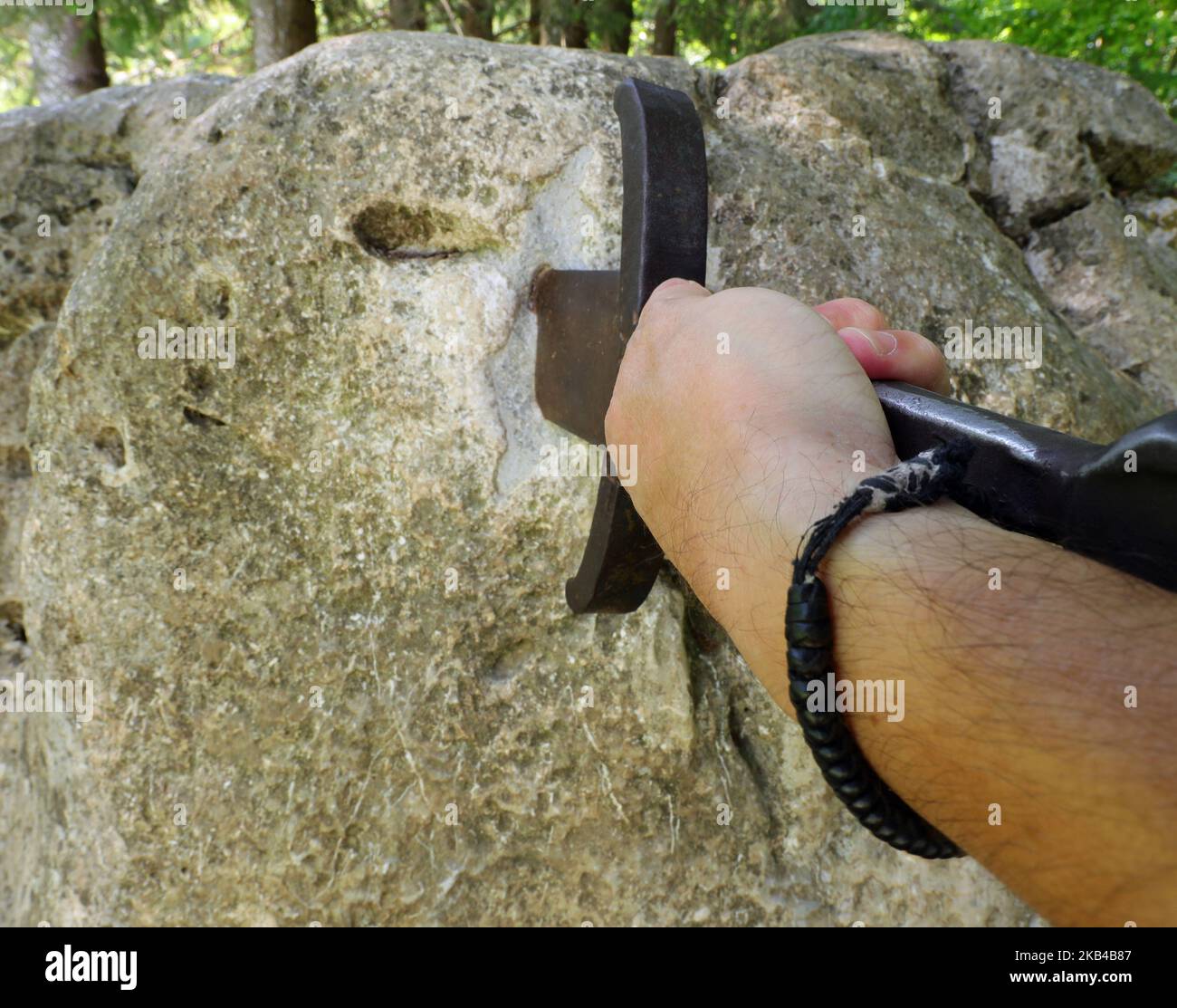 hand of the young man who forcibly tries to extract the sword Excalibur is stuck in the rock like King Arthur Stock Photo