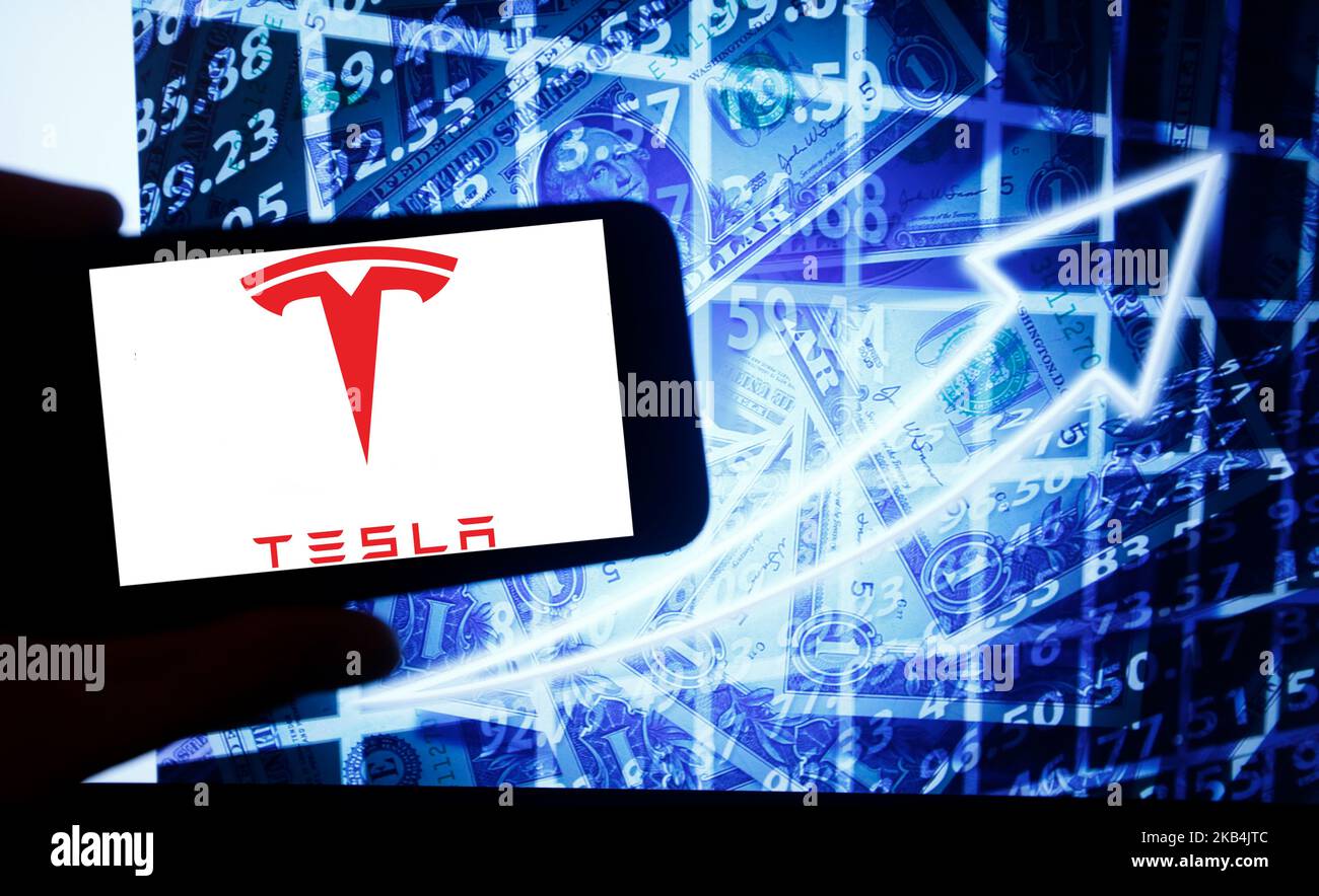 The logo of the Tesla Inc is seen on a screen of a smartphone next to a screen with an illustration ofthe stock market. Tesla is listed in Nasdaq. The Nasdaq is the second-largest stock exchange in the world after the New York Stock Exchange. (Photo by Alexander Pohl/NurPhoto) Stock Photo