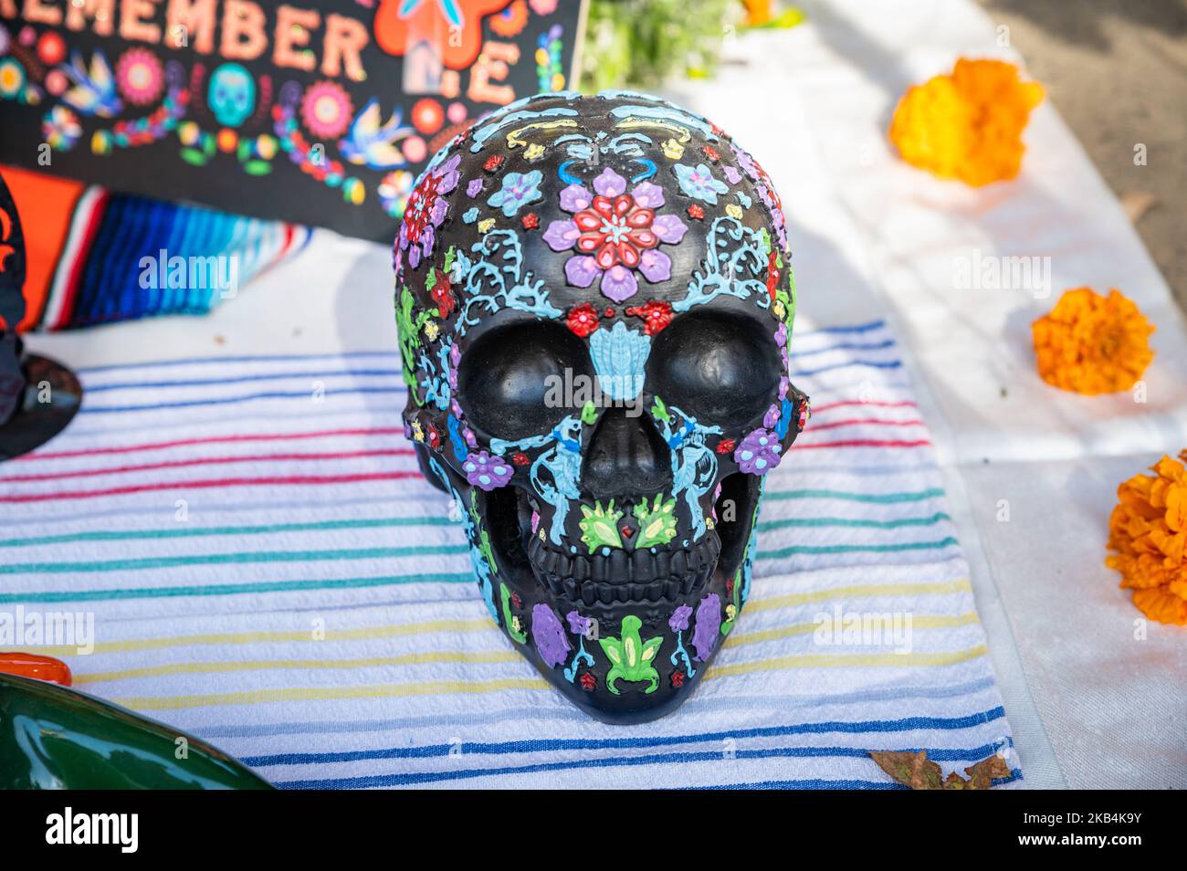 A colorful painted skull with marigold flowers and a Remember Me sign in the background are on an altar area as part of a Dia de los Muertos festival Stock Photo
