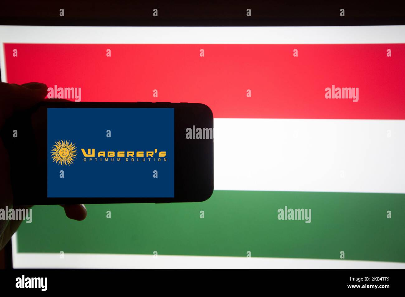 The logo of Waberer's International is seen on a screen of a smartphone in front of a hungarian flag. It is part of the BUX, the major index of Hungary. (Photo by Alexander Pohl/NurPhoto) Stock Photo
