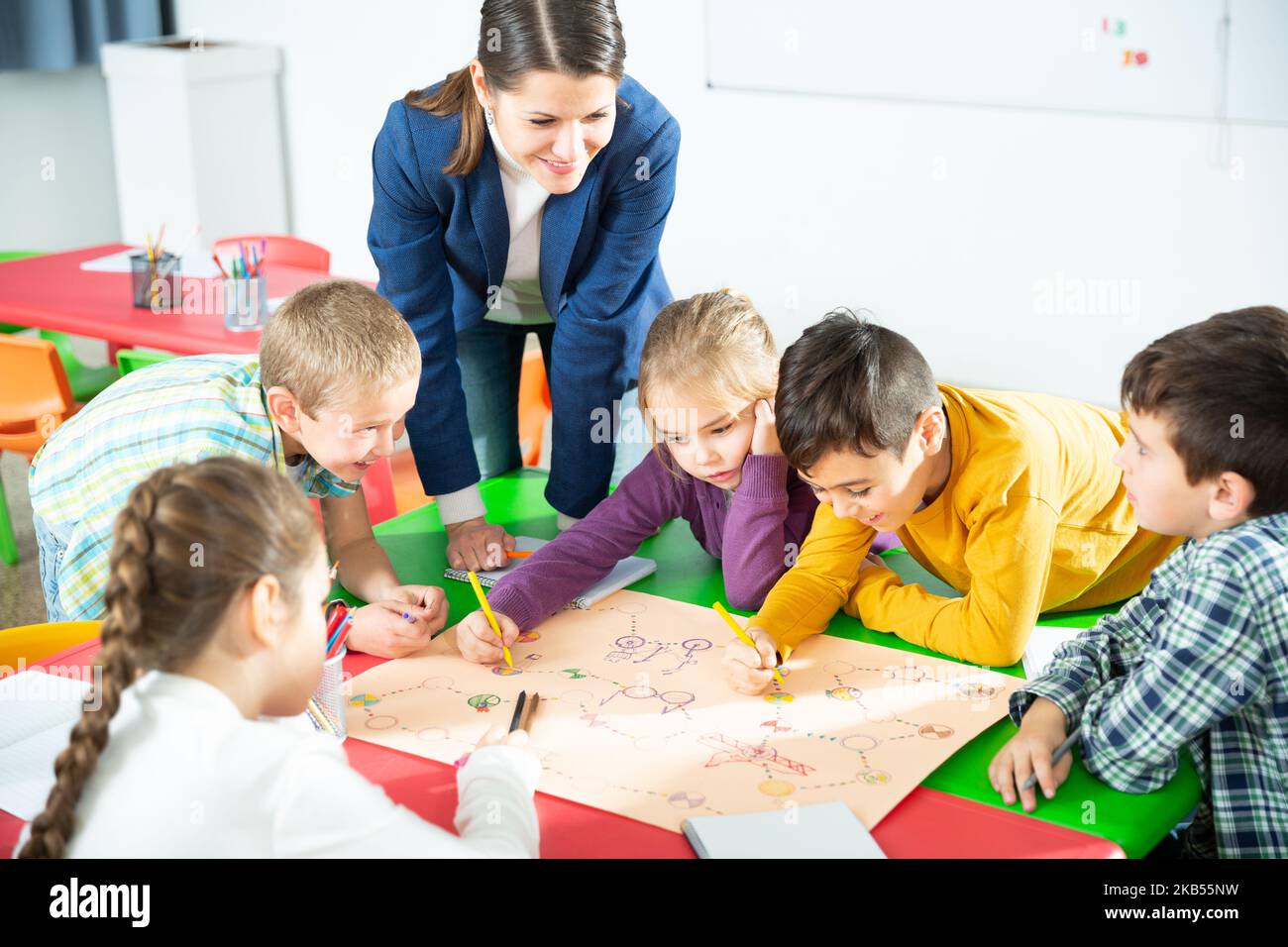 Teacher and collective of elementary age children draw together a board ...