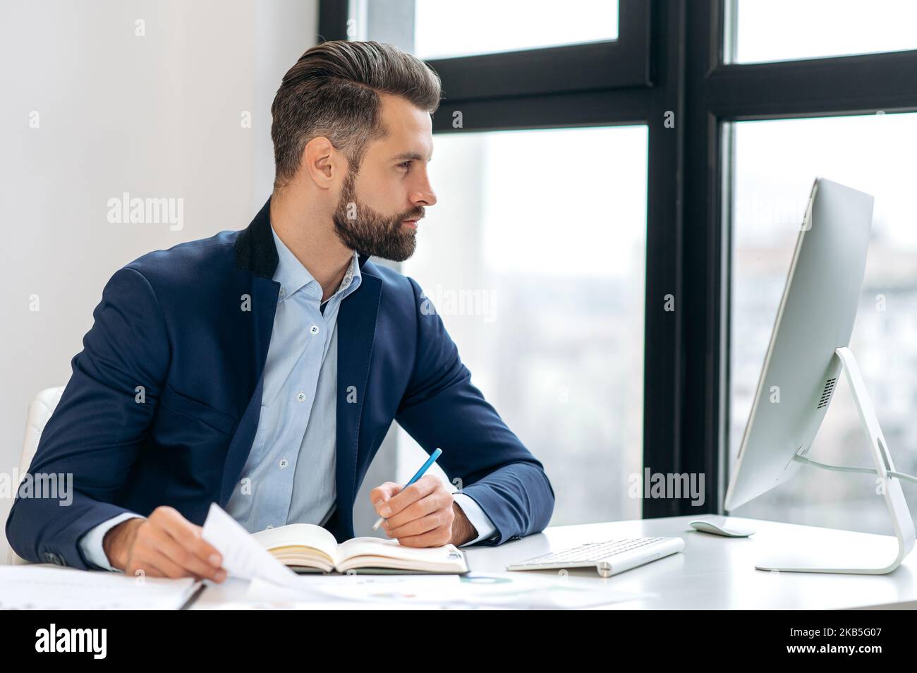 Focused successful confident caucasian businessman, in a suit, ceo, financial director, sits at a work desk, looks at computer screen, analyzes the company's financial profit, develop strategy Stock Photo