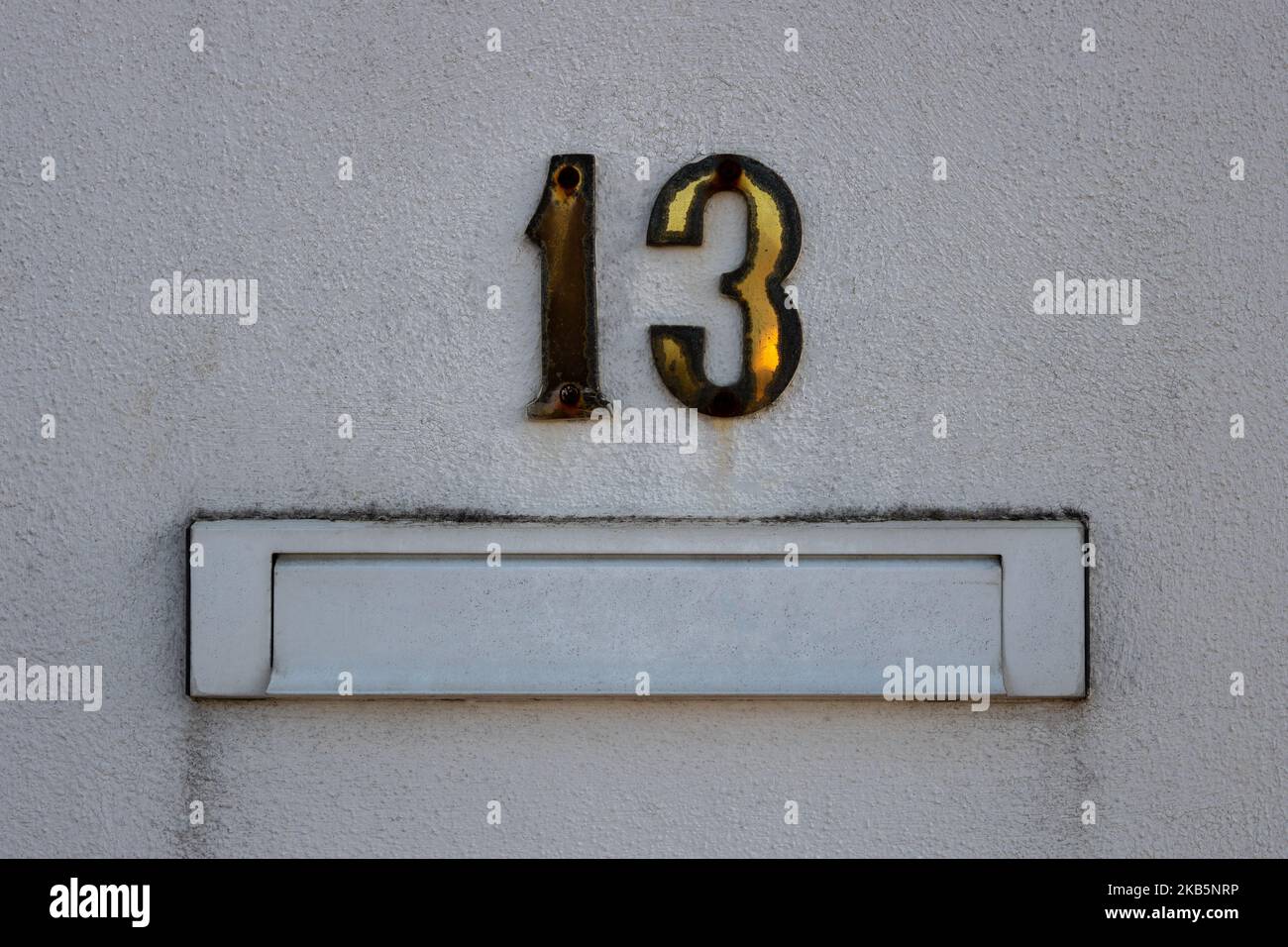 Closeup of white mailbox for letters and the number 13 (thirteen) on the exterior rough wall of