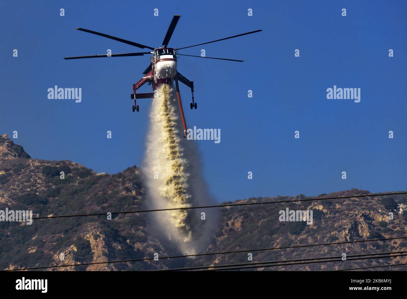 A firefighting helicopter makes a water drop on a wildfire in Altadena