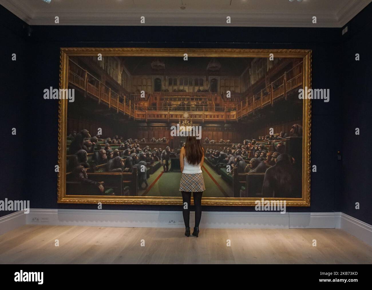 A gallery worker poses with the Banksy painting 'Devolved Parliament' at Sotheby's on September 27, 2019 in London, England. Photo call for Banksy's Devolved Parliament painting ahead of it being offered at auction by Sotheby's. The artwork showing the House of Commons full of chimpanzees is expected to fetch GBP1.5 to GBP2 million. (Photo by Giannis Alexopoulos/NurPhoto) Stock Photo