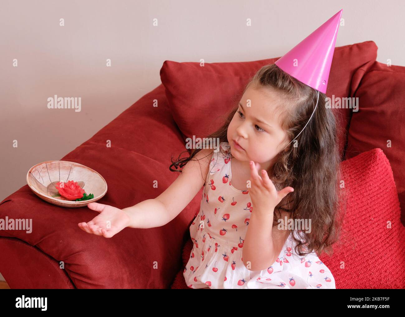 little girl in a party hat eating cake at her brother's first birthday