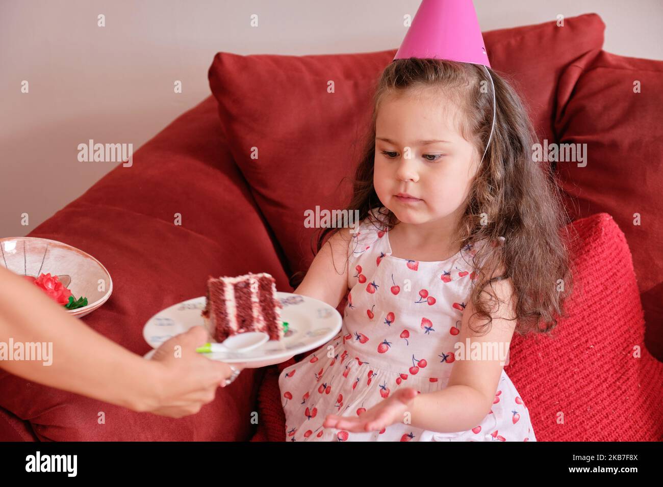 little girl in a party hat eating cake at her brother's first birthday
