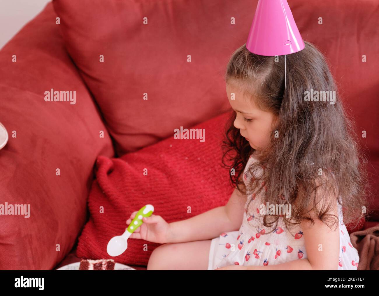 little girl in a party hat eating cake at her brother's first birthday