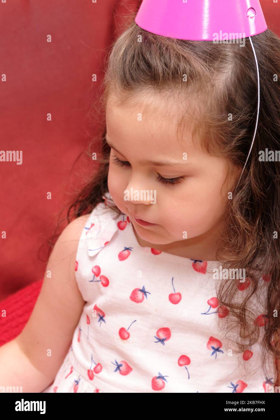 little girl in a party hat eating cake at her brother's first birthday
