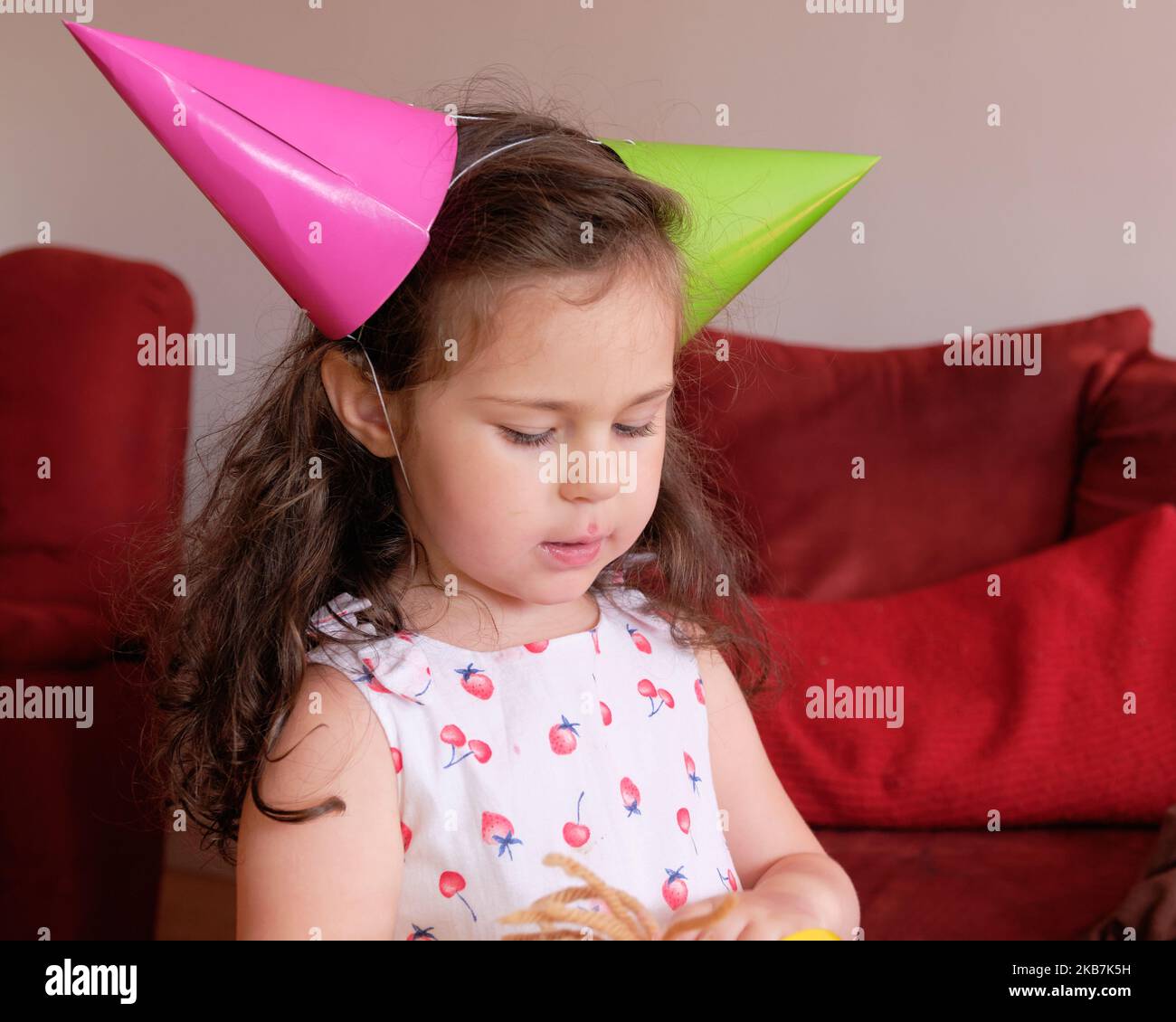 little girl in a party hat eating cake at her brother's first birthday