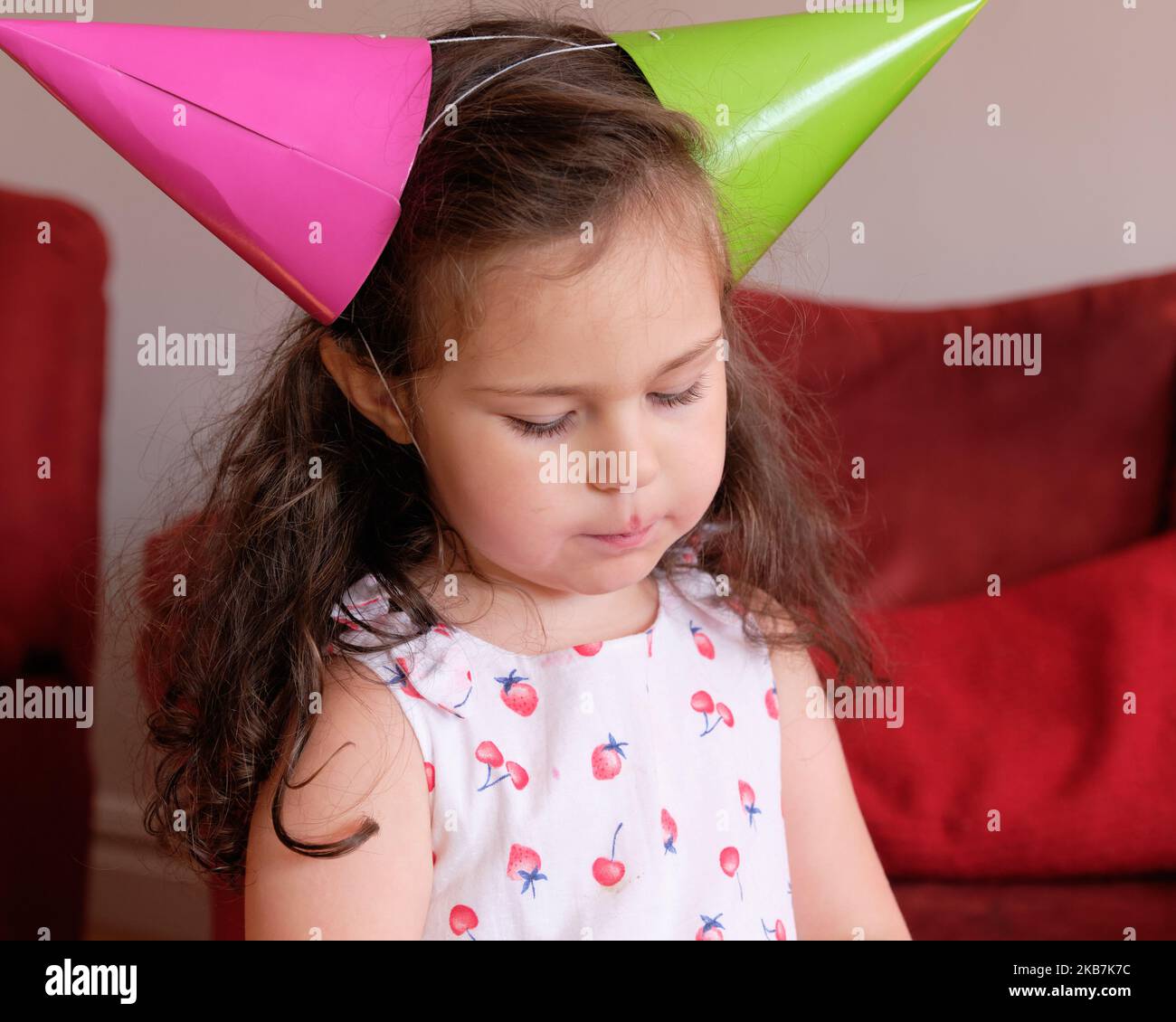 little girl in a party hat eating cake at her brother's first birthday