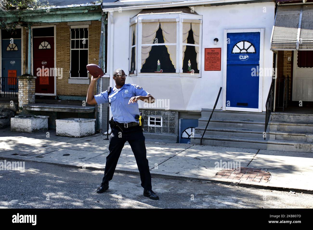 A police officer trows a football during a community block party, against a backdrop of the site of the August police stand-off, in the Nicetown-Tioga section of Philadelphia, PA, seen on October 15, 2019. (Photo by Bastiaan Slabbers/NurPhoto) Stock Photo
