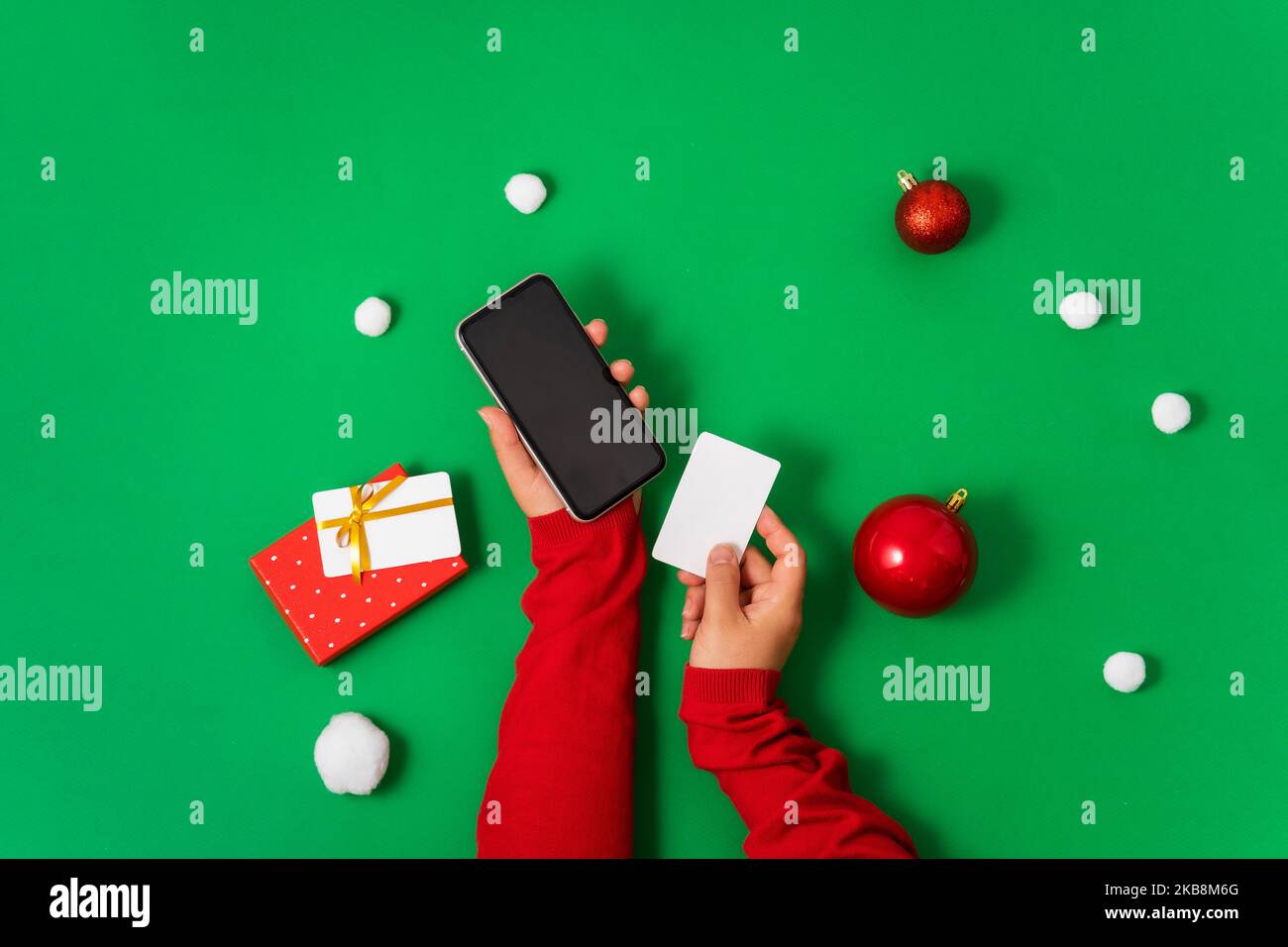 Female hands hold a smartphone and a bank card on a green background, Christmas decor and gifts. Flat lay, minimal Concept of online payment online sh Stock Photo