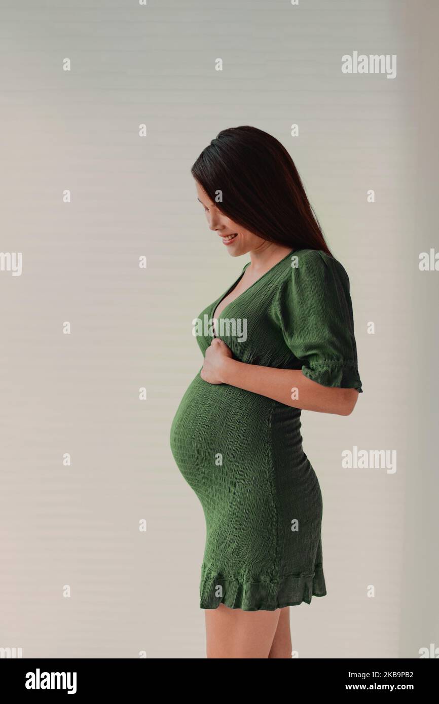 Pregnancy photoshoot beautiful pregnant woman model profile wearing dress to show baby bump on maternity shoot. Vertical portrait in studio Stock Photo