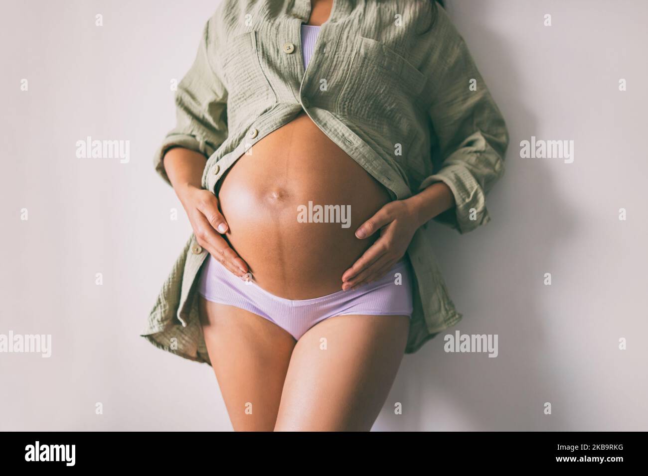 Pregnancy belly closeup. Pregnant woman wearing underwear and casual cotton shirt at home relaxing holding expecting tummy for skincare, health Stock Photo