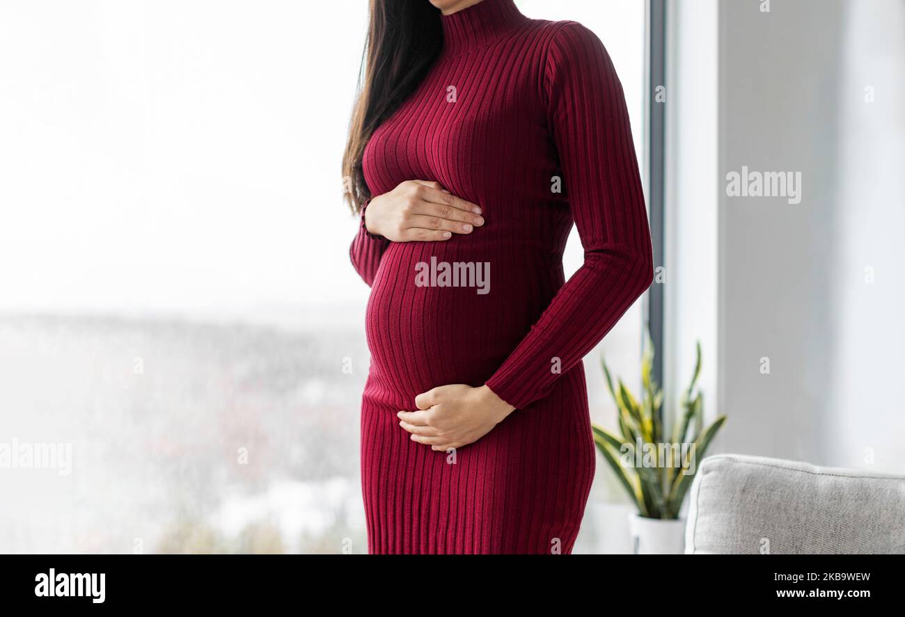 Pregnant woman profile holding her belly in red dress. Beautiful model for pregnancy maternity clothes Stock Photo