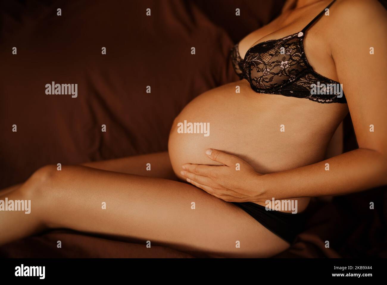 Pregnant woman pregnancy boudoir photoshoot in black lace underwear dark background. Profile body crop of lady touching expecting baby bump Stock Photo
